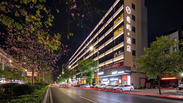 Um hotel de vários andares com fachada moderna, sinalização iluminada e área de estacionamento com carros.