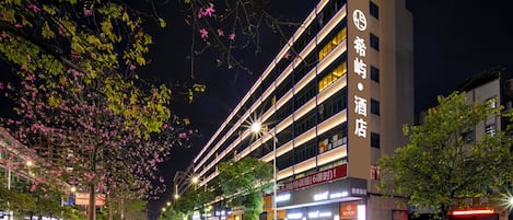 Un hôtel à plusieurs étages, doté d’une façade moderne, d’une enseigne lumineuse et d’un parking où sont stationnées des voitures.