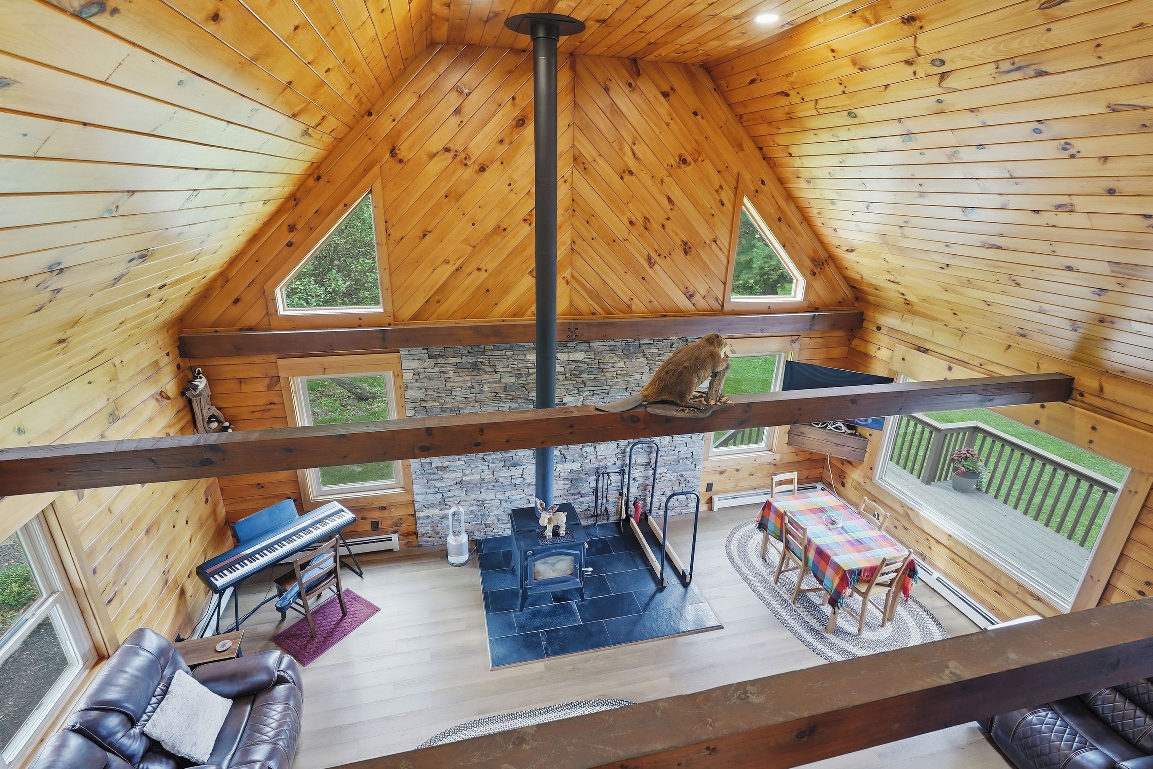 L’intérieur d’un chalet en bois, avec une cheminée en pierre, un piano, un canapé et un coin repas.
