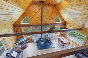 A wooden cabin interior with a stone fireplace, a piano, a sofa, and a dining area. - Secluded 3 Bedroom Cabin on 100 Acres (Canandaigua)