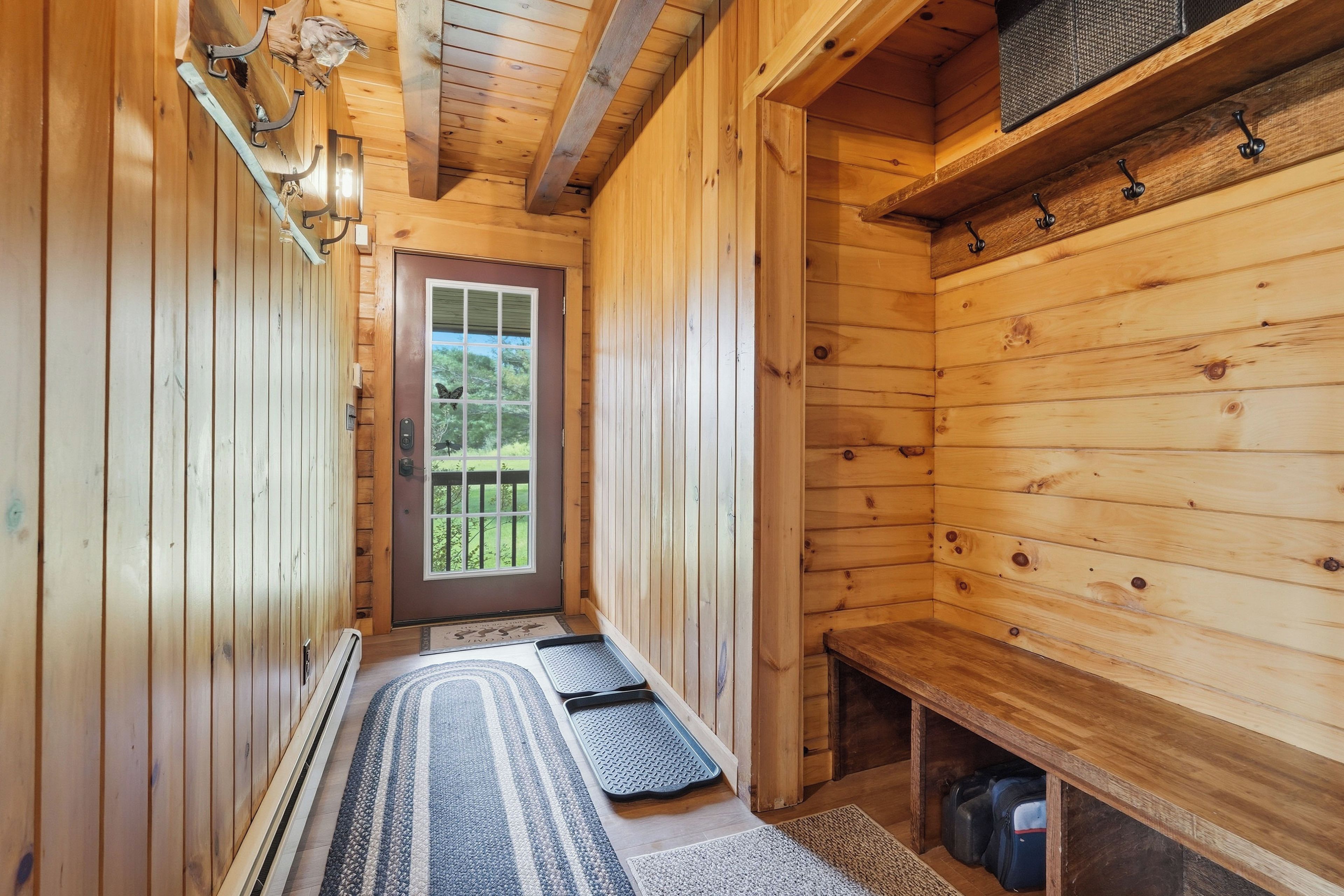 A wooden interior with a door leading outside, a bench, and a bench seat.