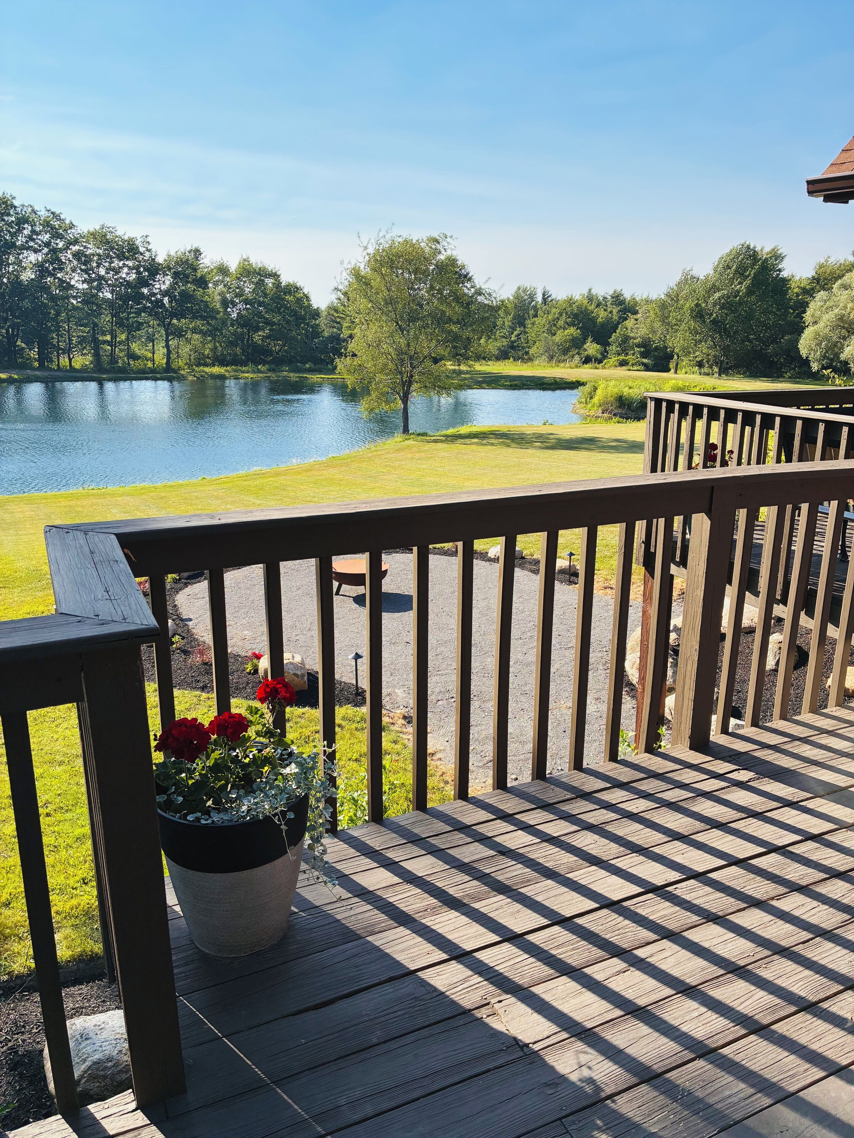 Une terrasse en bois avec une rambarde donnant sur un lac et une zone herbeuse.