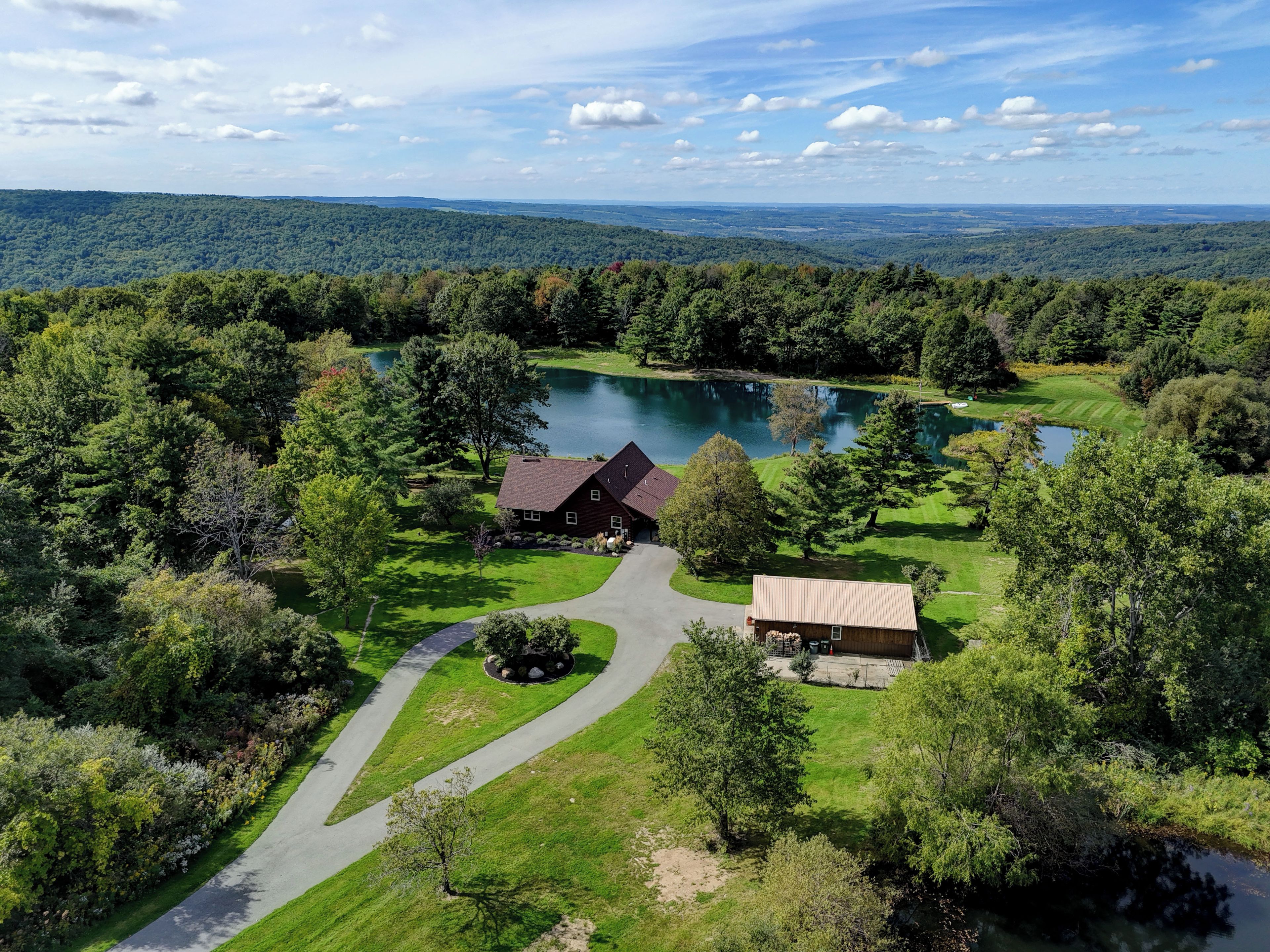 Una casa grande rodeada por un lago y un bosque frondoso, bajo un cielo despejado.