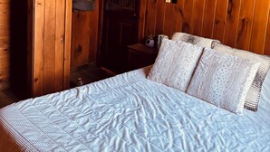 Ein Interieur einer Holzhütte mit einem Bett, einer Holzhängeleuchte und einer Tür.