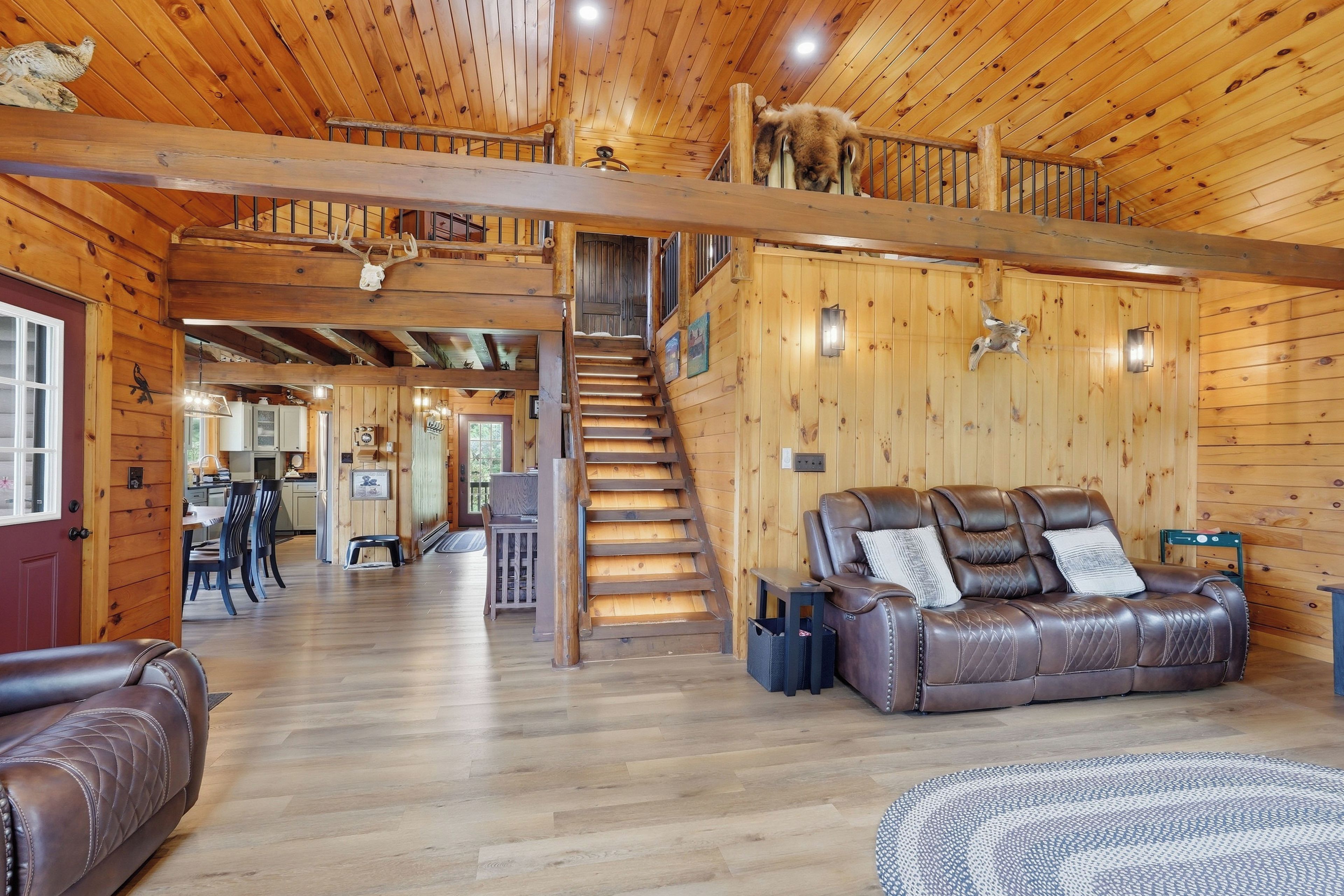 A spacious log cabin interior with a loft bedroom, a dining area, and a leather sofa.