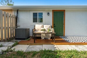 Ein Wohnhaus mit Terrasse, einer grünen Tür, einem weißen Zaun und einem kleinen Fenster.