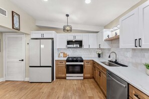 Eine moderne Küche mit weißen Schränken, einem Edelstahlkühlschrank, einem eingebauten Backofen und einem Geschirrspüler.