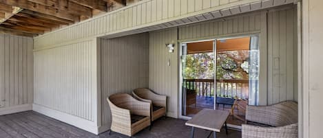 A covered outdoor area with wooden flooring, wicker furniture, and a sliding glass door leading to an outdoor deck.