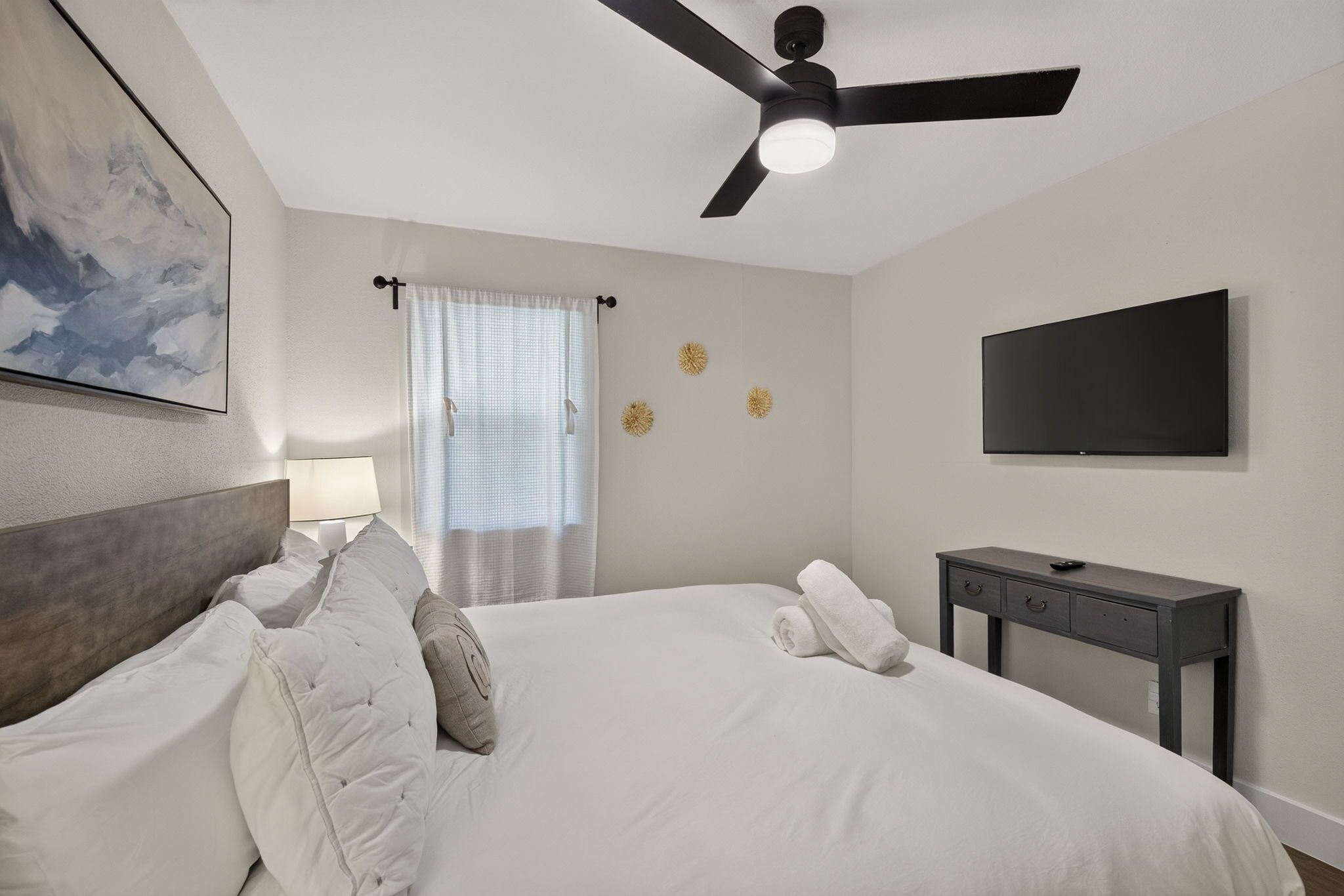 Une chambre d’hôtel avec un lit, un ventilateur de plafond, une télévision, une table de chevet et une fenêtre avec des rideaux.