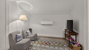 A small, modern living room with a sofa, a lamp, an air conditioning unit, a television, and a patterned rug.