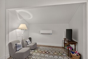 A small, modern living room with a sofa, a lamp, an air conditioning unit, a television, and a patterned rug.