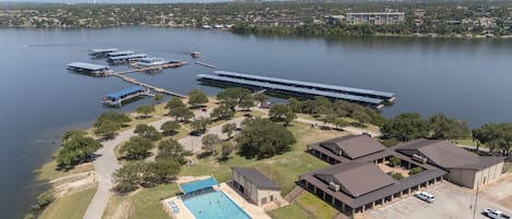 Vista aérea de una propiedad junto al lago con piscina, zona de estacionamiento y varias edificaciones.