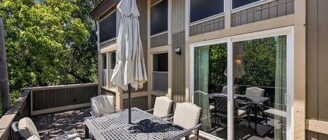 An outdoor patio with a table and chairs, a covered umbrella, and a view of the backyard through large sliding glass doors.
