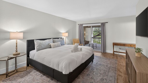 A modern bedroom with a large bed, bedside lamps, a desk, and a view of the outdoors.