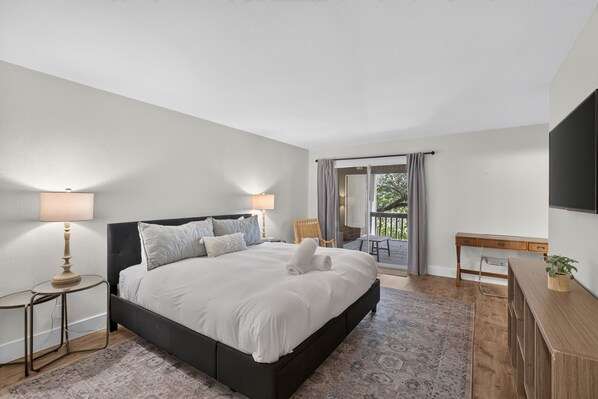 A modern bedroom with a large bed, bedside lamps, a desk, and a view of the outdoors.