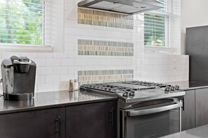 Une cuisine moderne équipée d’une cuisinière à gaz intégrée, d’une machine à café et d’une fenêtre avec des stores.