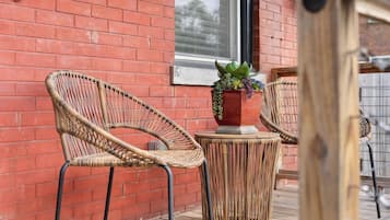 Wicker chairs and a table on a wooden deck with a red brick wall in the background.