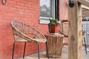Wicker chairs and a table on a wooden deck with a red brick wall in the background. - Olive & Brick | Hot Tub • Private Backyard Oasis (Cincinnati)