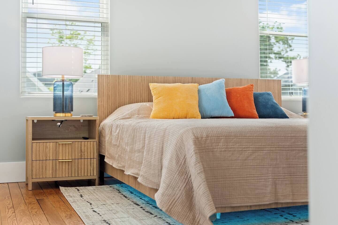 Une chambre à coucher avec un lit, une table de chevet, une lampe et une vue sur l’extérieur.