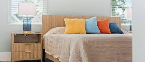 A bedroom with a bed, bedside table, lamp, and a view of the outdoors.