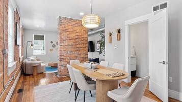 A modern dining area with a brick accent wall, a wooden dining table, and white chairs.