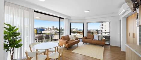 A modern apartment with a balcony, a dining area, and a living room with a sofa and chairs.