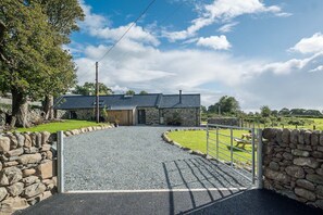 A stone building with a gravel driveway leading to a gated entrance. - Luxury Two Bedroom Holiday Cottage with Hot Tub and Sea Views | Y-Ddol (Dyffryn Ardudwy)