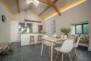 A modern kitchen with a central island, wooden stools, and a dining table with chairs. - Luxury Two Bedroom Holiday Cottage with Hot Tub and Sea Views | Y-Ddol (Dyffryn Ardudwy)
