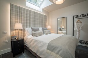 A bedroom with a bed, bedside lamps, a radio, a mirror, and a clothing rack. - Luxury Two Bedroom Holiday Cottage with Hot Tub and Sea Views | Y-Ddol (Dyffryn Ardudwy)