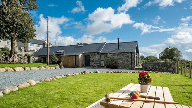 A stone building with a sloped roof, a gravel driveway, and a picnic table with a ball and croquet mallets. - Luxury Two Bedroom Holiday Cottage with Hot Tub and Sea Views | Y-Ddol (Dyffryn Ardudwy)
