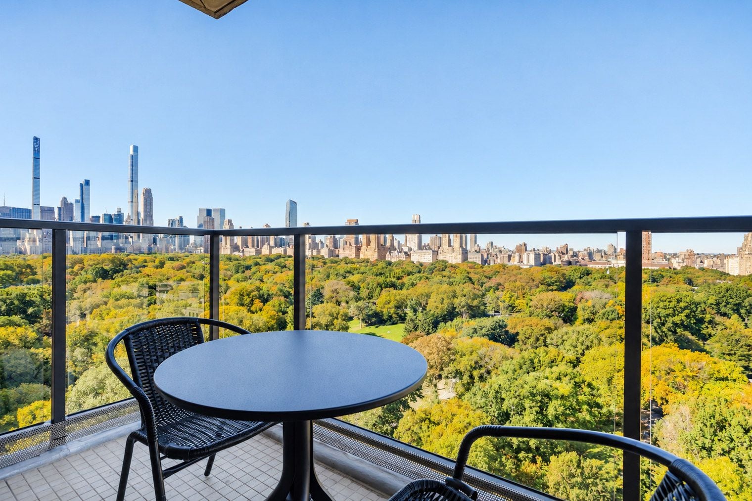 A balcony with a table and chairs, overlooking a cityscape and a park.