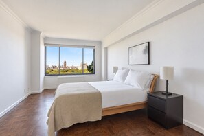 A bedroom with a large window, a bed, a nightstand, and a lamp. - Blueground | Upper East Side, terrace, nr MET (New York)