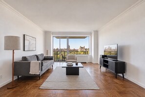 A modern living room with a sofa, coffee table, and TV, featuring a large window with a city view. - Blueground | Upper East Side, terrace, nr MET (New York)