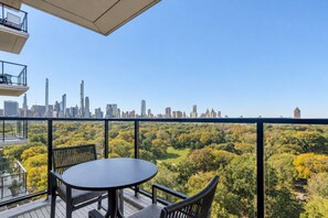 A balcony with a table and chairs, overlooking a city skyline and a forested area. - Blueground | Upper East Side, terrace, nr MET (New York)
