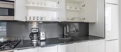 Et moderne køkken med hvide skabe, komfur i rustfrit stål, kaffemaskine og vask.