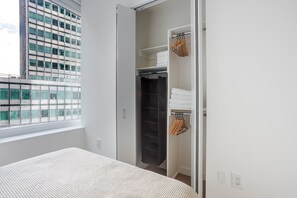A bedroom with a bed, a closet with hanging space, and a window with a view of a building. - Blueground | Financial District, rooftop pool, nr Brooklyn Bridge (New York)