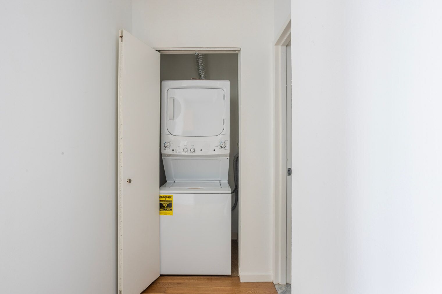 A laundry room with a washer and dryer, a yellow energy efficiency label, and a wooden floor.