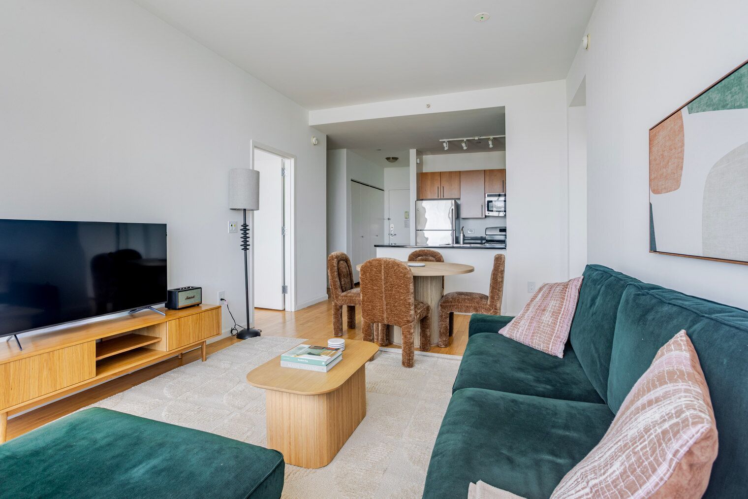 A modern living room with a flat-screen TV, wooden entertainment unit, green sofa, and a dining area with a table and chairs.
