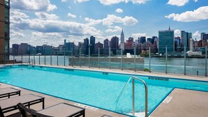 Piscina no terraço com vista para o horizonte urbano, incluindo um arranha-céu imponente.
