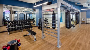 Uma academia com equipamentos de musculação, um banco e sacos de pancada.