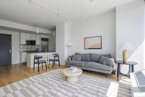 A modern living room with a grey sofa, a coffee table, and a dining area with a small island and chairs. - Blueground | Hell's Kitchen, view, nr Central Park (New York)