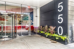 Una entrada moderna a un edificio con puerta giratoria de vidrio, una pared negra con el número 550, y plantas en macetas.