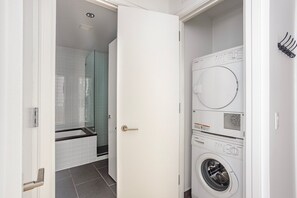Una sala amb bugaderia que disposa d'una rentadora de càrrega frontal, una assecadora, un envàs de dutxa de vidre i una porta blanca.