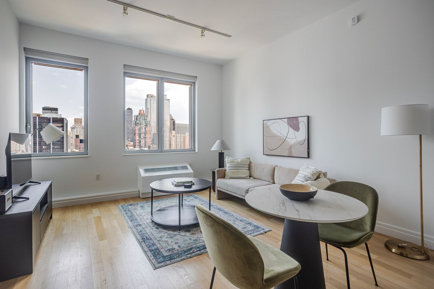 Ein modernes Wohnzimmer mit einer Couch, einem runden Tisch und Blick auf die Stadt durch große Fenster.