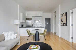 A modern living space with a sofa, a dining table with chairs, a kitchen area, and a door leading to another room. - Blueground | Hell's Kitchen, view, nr Times Square (New York)