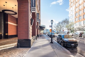 A hotel entrance with a brick facade, a covered walkway, and a parking area with cars. - Blueground | Manhattan, rooftop, nr Battery Park (New York)