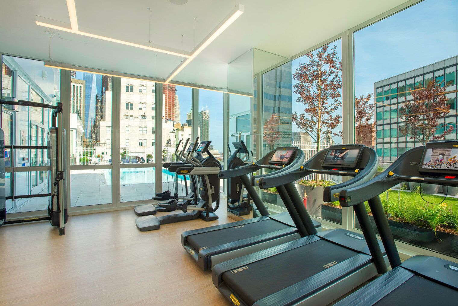 Ein modernes Fitnessstudio mit Laufbändern, Rudergerät und Ergobiczyklen, große Fenster mit Blick auf die Stadt.