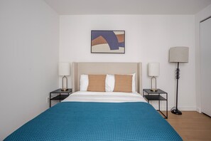Ein Hotelzimmer mit einem Bett, zwei Nachttischen, einer Stehlampe und einem an der Wand hängenden abstrakten Gemälde.