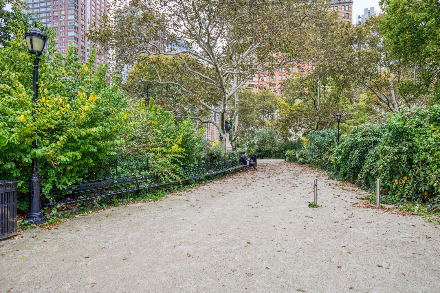 Ein Parkweg mit Bänken, umgeben von Bäumen und einem Zaun.