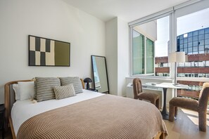A hotel room with a bed, a desk, a chair, and a large window offering a view of buildings. - Blueground | Financial District, rooftop pool, nr Brooklyn Bridge (New York)